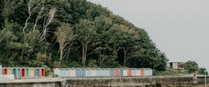 A line of colourful beach huts, with lush greenery behind them. Sandown Coast, Isle of Wight