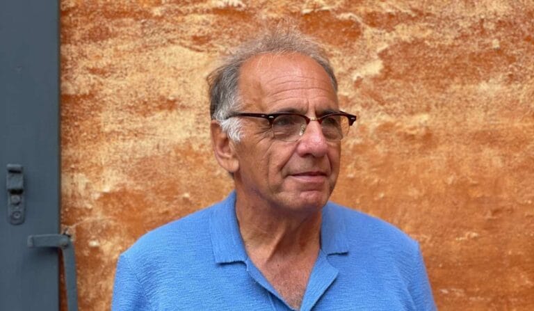 An image of Gavin Stride. He's wearing a bright blue shirt against a burnt orange background.