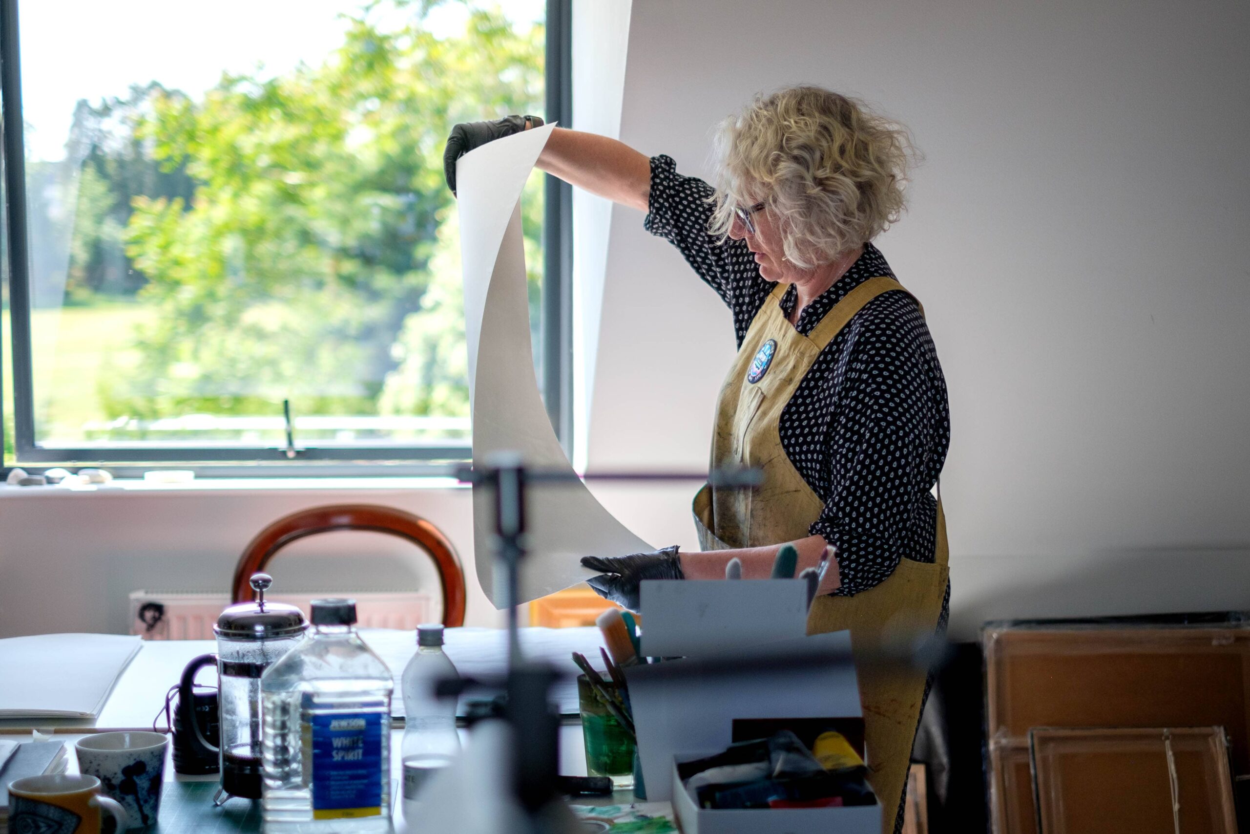 Photo of Fran in her studio, holding a large sheet of paper ready for print making.