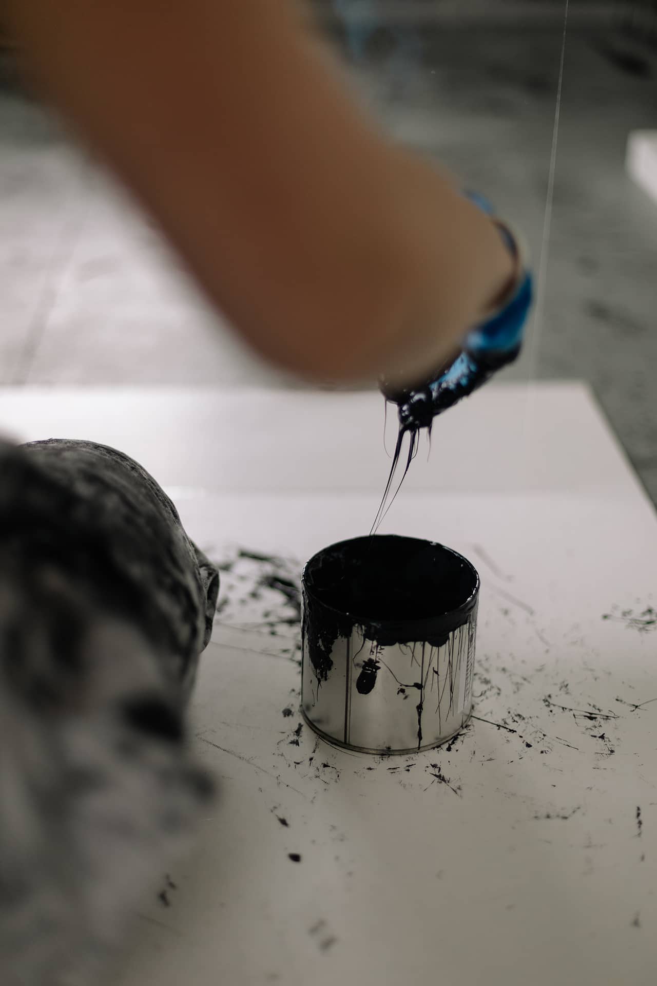 A black paint pot with an arm bringing the paintbrush out. There is some intended spillage on the canvas.