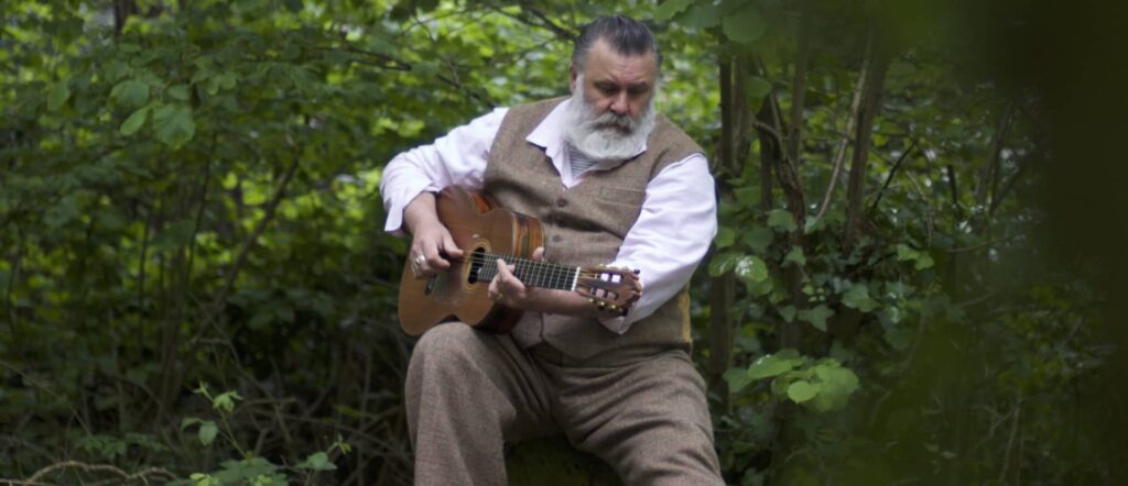 Paul Armfield sitting among the trees with his guitar