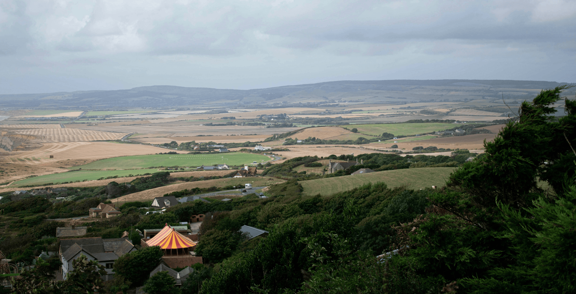 Drone landscape picture of the Isle of Wight. Lush greenery and a small, orange striped circus tent.