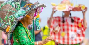 A lady wearing a vibrant green dress, wearing a homemade hat made from painted newspaper, wire and textile fabrics.