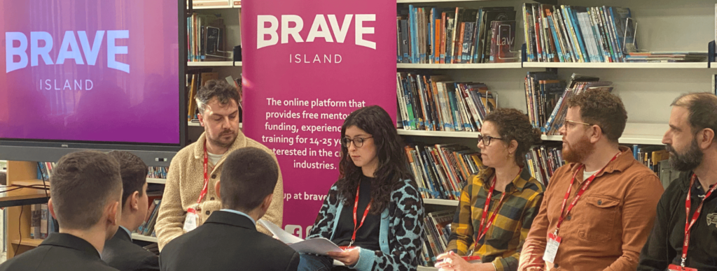 Young creatives from Brave Island sat in front of school students, with Brave Island branding behind them.