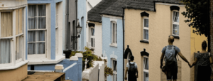 A view from a street in Cowes, two people holding hands walk in front of colourful houses.