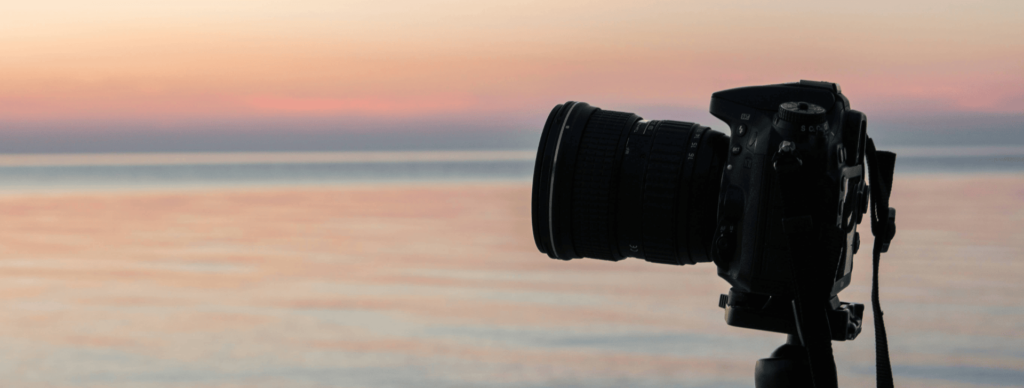 A camera overlooking a pink, orange sunset & beach horizon line.