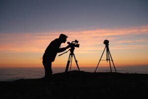 Person in silhoette with sunset in background taking photos from a tripod