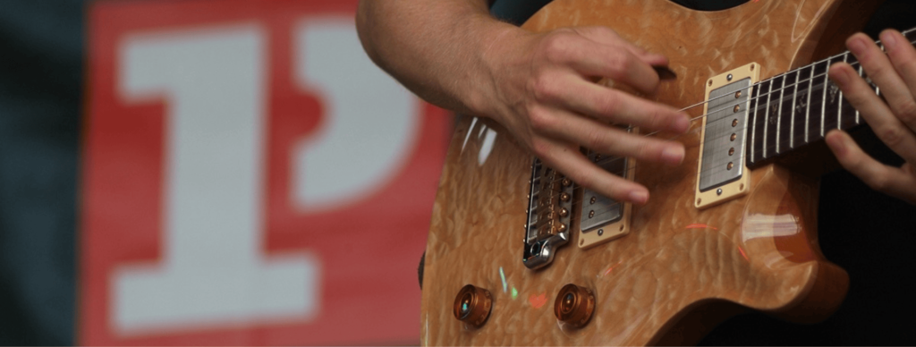 A close up image of someone playing the guitar, with a blurred Platform One logo in the background.