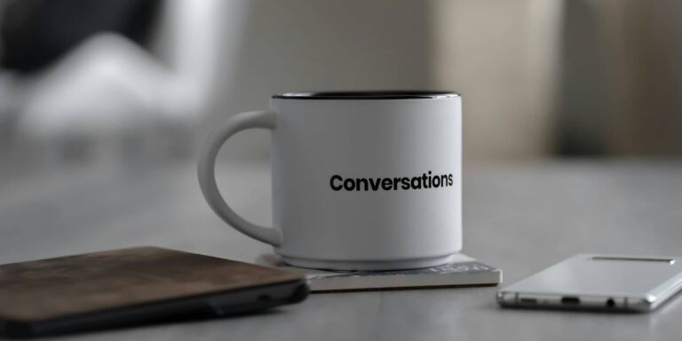 notepad, phone and cup on table with the word 'conversations' on it