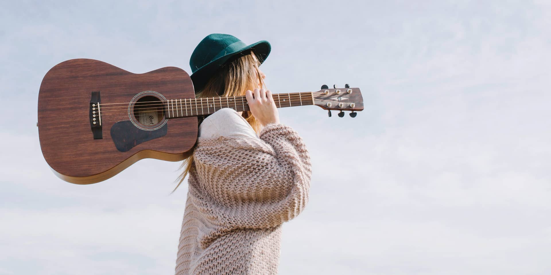 Woman walking through field holding guitar over her shoulder