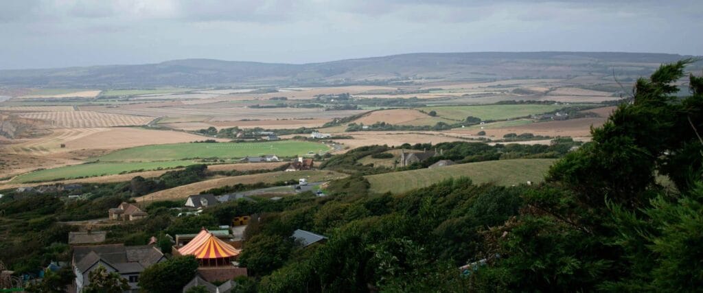 Drone landscape picture of the Isle of Wight. Lush greenery and a small, orange striped circus tent.