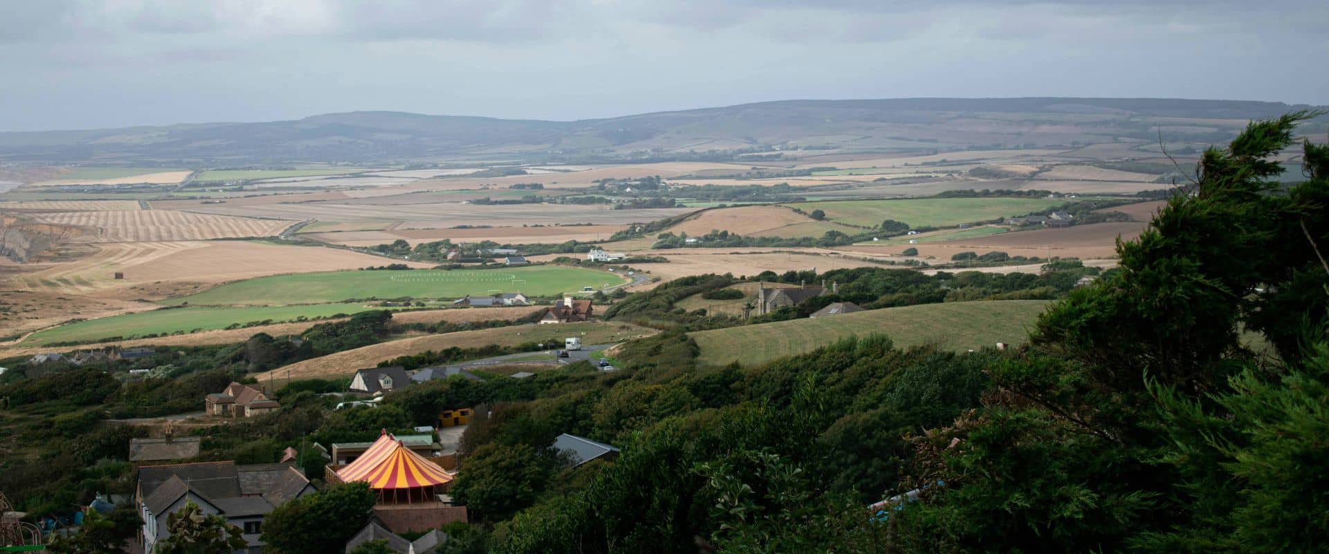 Drone landscape picture of the Isle of Wight. Lush greenery and a small, orange striped circus tent.