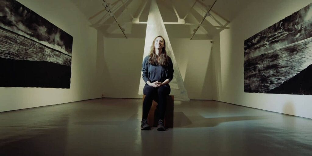 A centered Caroline smiles as she's inbetween two of her art pieces.