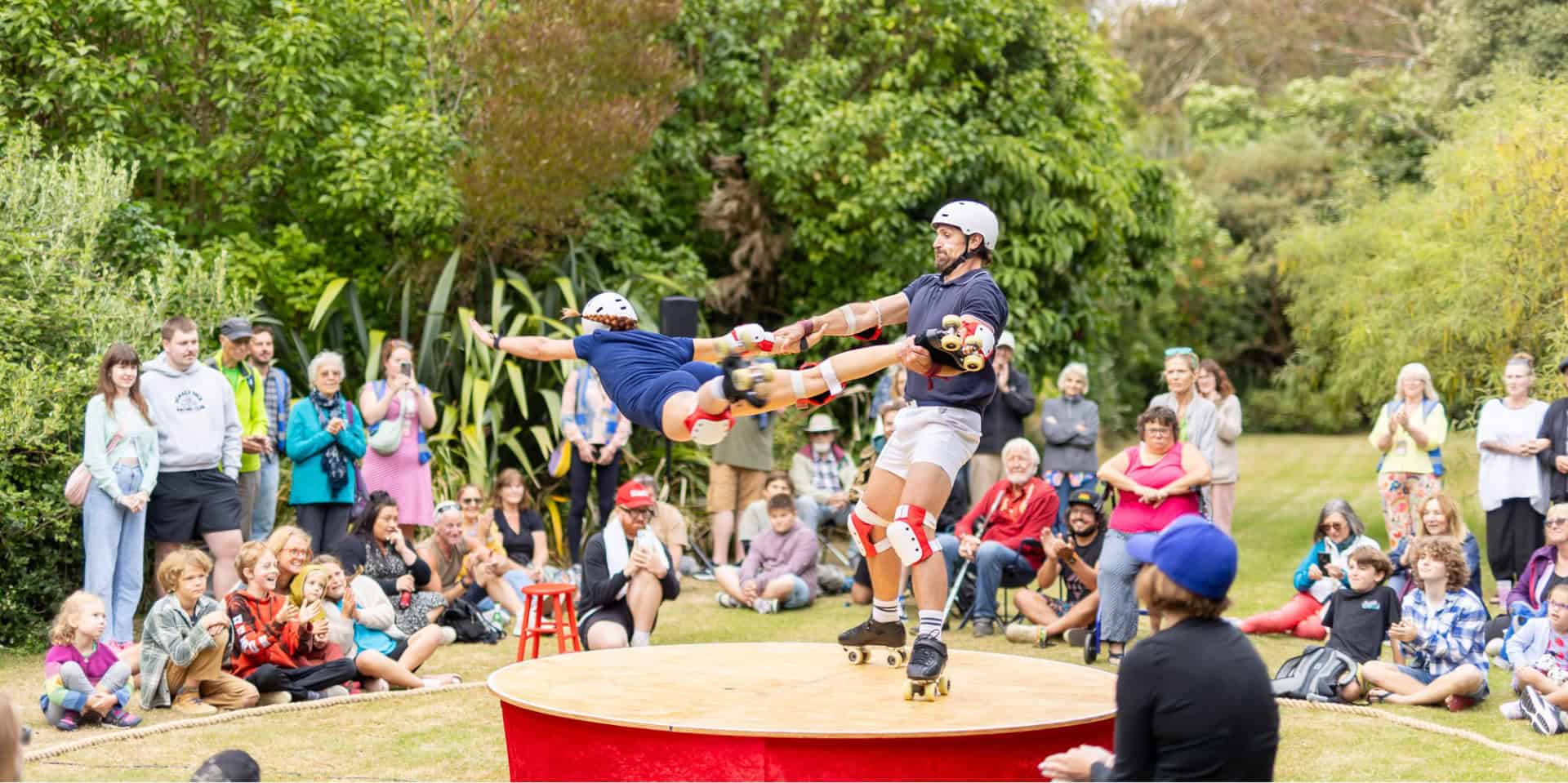 Two roller skating acrobats on a small circular stage with one spinning the other around by holding onto their wrist and ankle