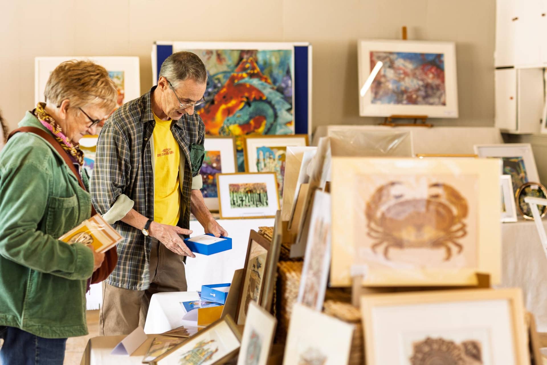 A man and a woman looking through piles of artworks for sale 