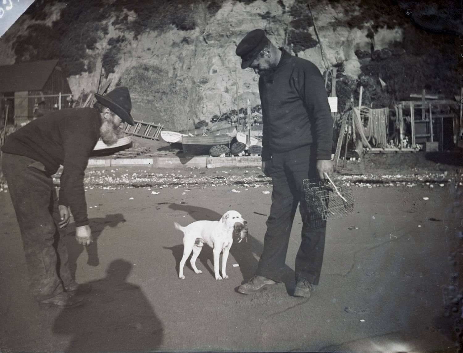 Black and white photo of two longshoremen with a dog that has a rat in its mouth