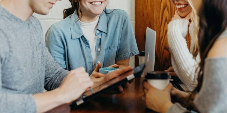 four young people in a meeting with coffee cups and laptops
