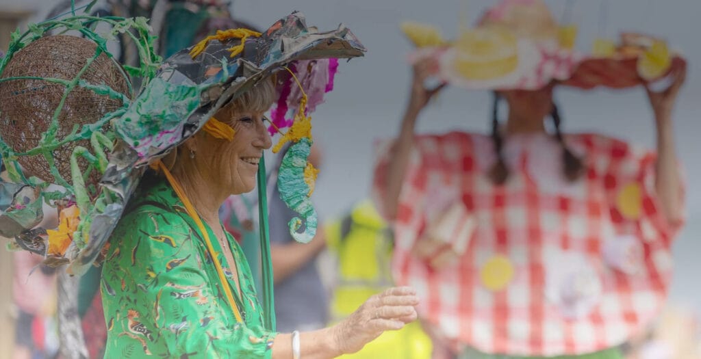 A lady wearing a vibrant green dress, wearing a homemade hat made from painted newspaper, wire and textile fabrics.