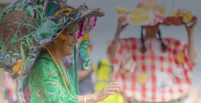 A lady wearing a vibrant green dress, wearing a homemade hat made from painted newspaper, wire and textile fabrics.