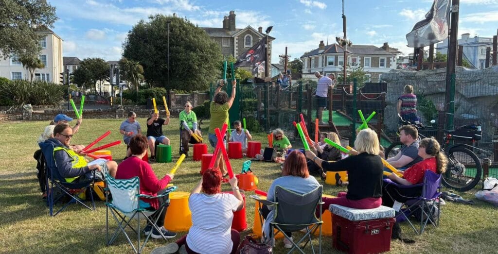 A group sat in a circle with drums and sound tubes on a sunny day in Ryde.