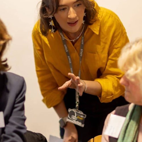 A young woman in a yellow shirt talking and helping others.