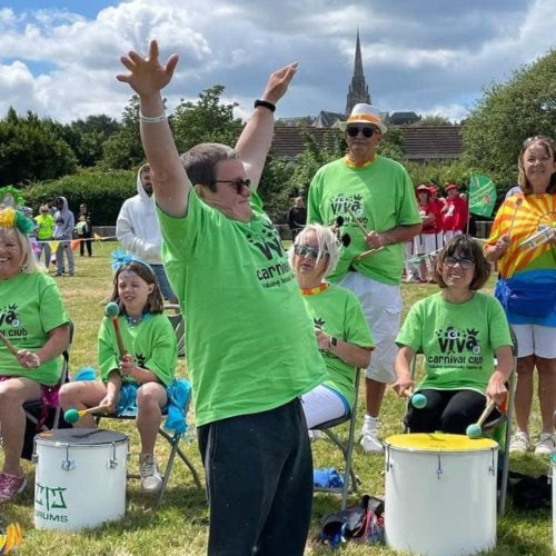 Viva Carnival members with drums in Ryde. A young lad at the front is dancing with his arms up in the sky!